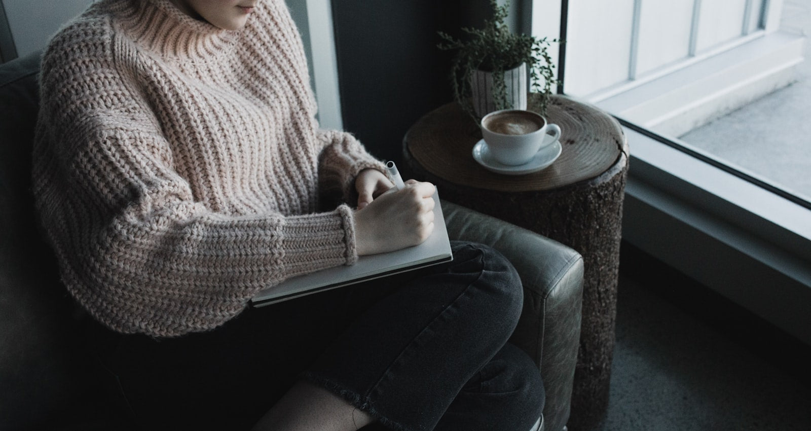 A woman writing in a journal by a window with coffee instead of reaching for a phone